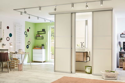 Modernes Zimmer mit weißen Schiebetüren aus Holz und integriertem Bad mit Waschbecken und Spiegel.