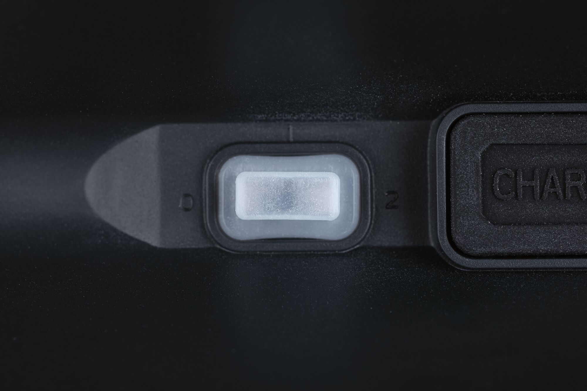 Close-up of white plastic switch on black casing with charging port next to it