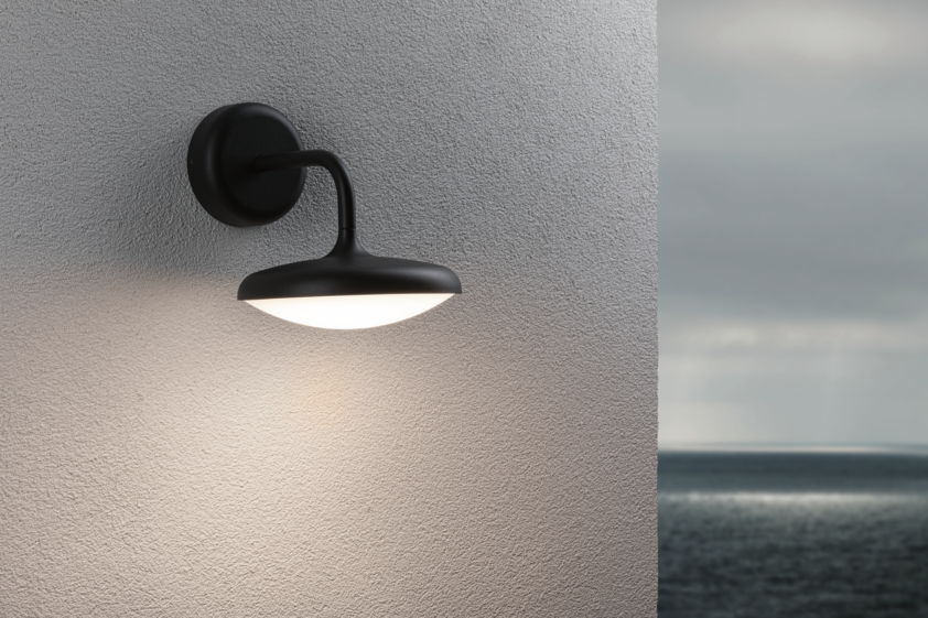 Schwarze Außenwandleuchte aus Metall mit rundem, weißem Diffusor und warmweißem Licht am Haus.