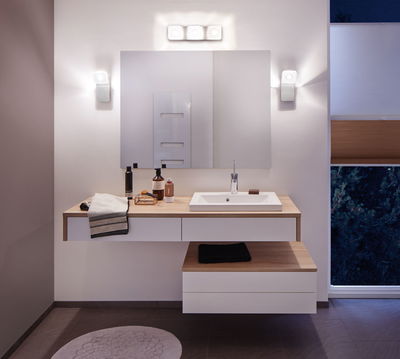 Modernes Badezimmer mit weißem Waschbecken, Holzarbeitsplatte und warmweißen LED-Wandleuchten