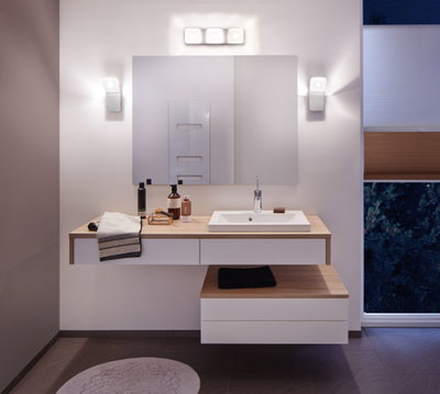 Modernes Badezimmer mit weißem Waschbecken, Holzarbeitsplatte und warmweißen LED-Wandleuchten