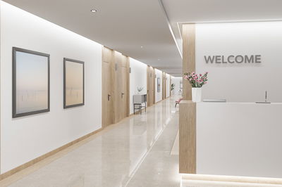 Moderne reception med hvidt skrivebord, trædetaljer og LED-loftlys i gang.