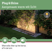 Buitenverlichting met warm wit licht op stenen muur met planten in een tuin