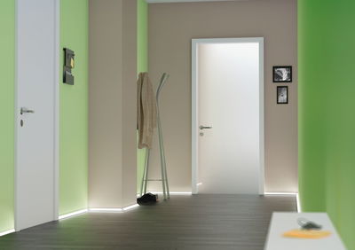 Moderner Flur mit weißen Türen, grünen Wänden und LED-Bodenbeleuchtung für stimmungsvolles Licht.
