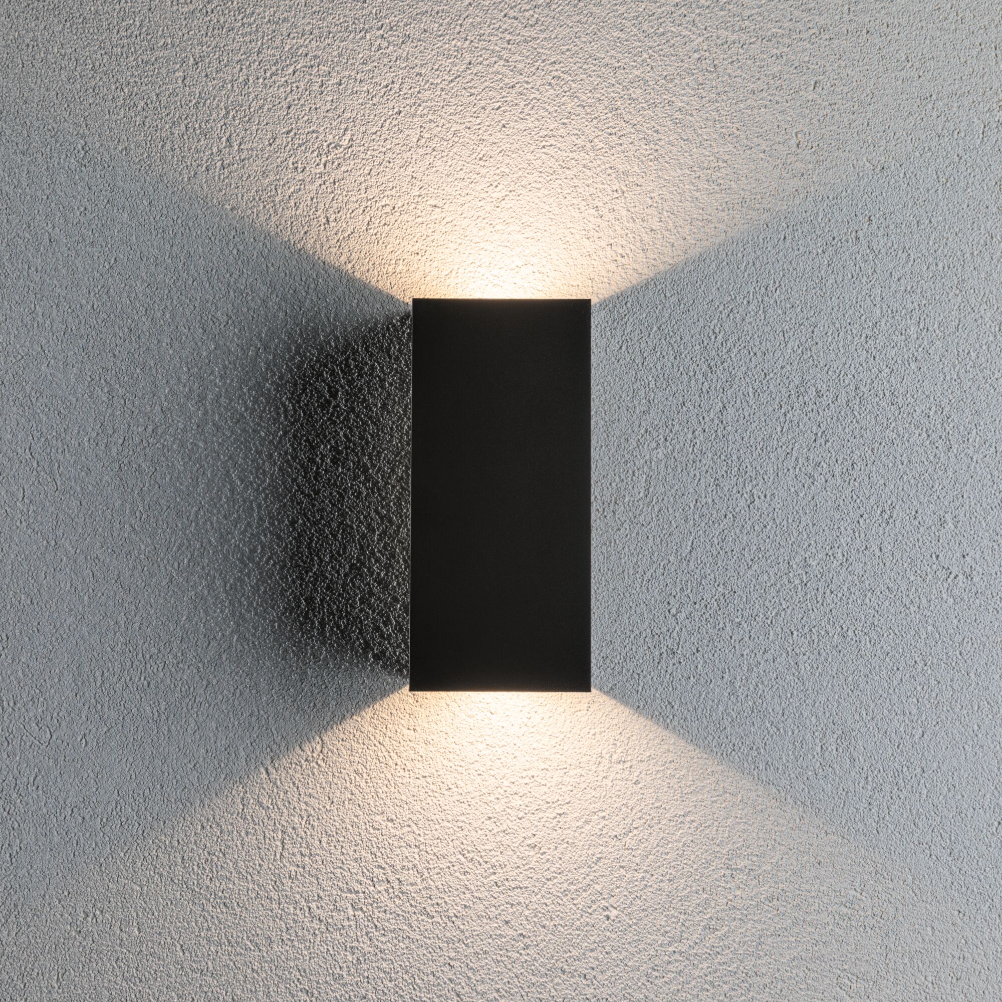 Black rectangular metal LED wall light with warm white light on grey wall for modern indoor lighting