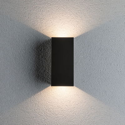 Zwarte rechthoekige metalen LED-wandlamp met warm wit licht op grijze muur voor moderne binnenverlichting