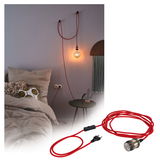 Red textile cable with switch and bulb socket, stylishly mounted on bedroom wall for lighting.