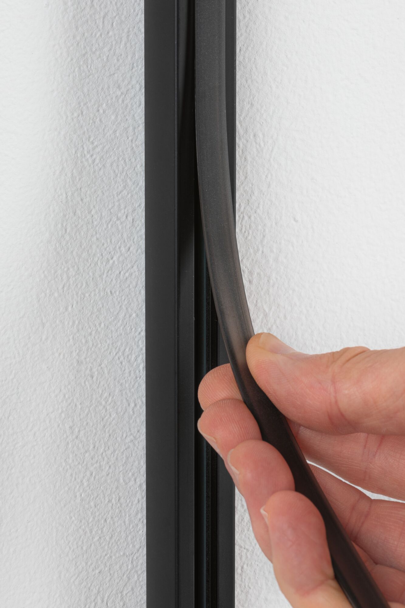 Hand hält schwarzen flexiblen Dichtungsstreifen aus Gummi an weißer Wand für Abdichtung
