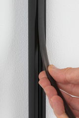 Hand hält schwarzen flexiblen Dichtungsstreifen aus Gummi an weißer Wand für Abdichtung