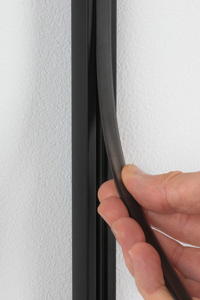 Hand holding black flexible rubber sealing strip against white wall for insulation