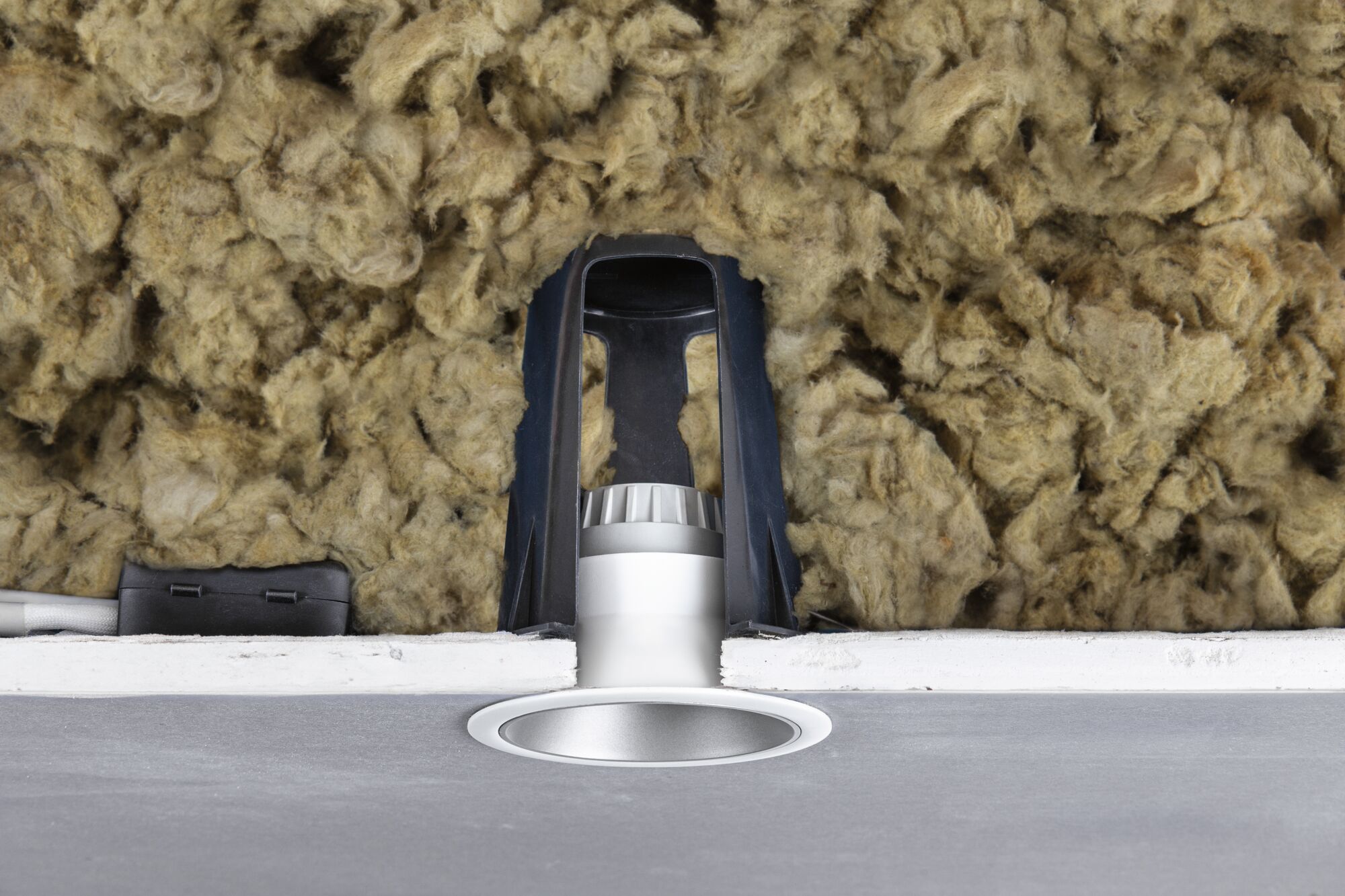Silver recessed LED spotlight with black bracket and insulation in ceiling cavity for energy-efficient lighting
