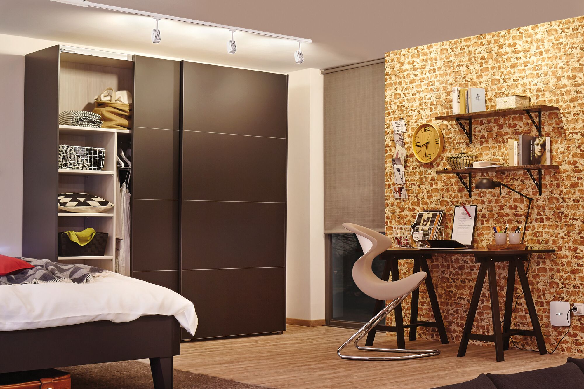 Modernes Schlafzimmer mit dunklem Holzkleiderschrank, Schreibtisch und Stuhl vor Ziegelwandbeleuchtung