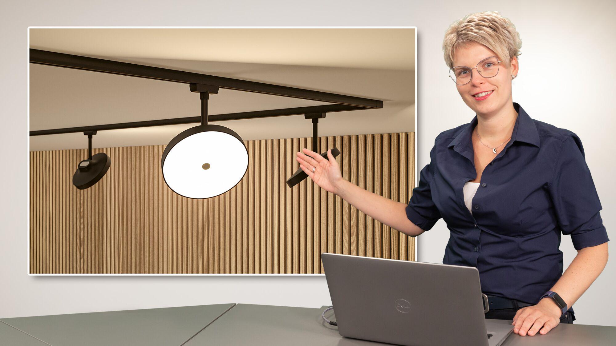 Femme présentant un système d'éclairage sur rail URail noir à LED devant un panneau en bois en webinaire.