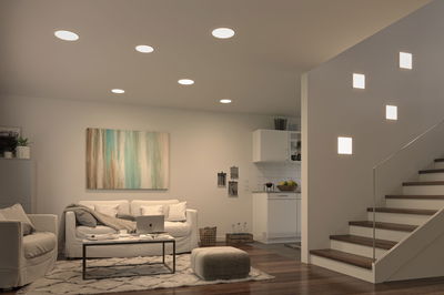 Modern living room with white recessed ceiling lights and square wall lamps on stairs, wooden floor