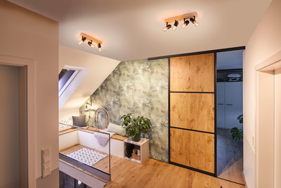 Moderner Wohnraum mit Holzdeckenstrahlern, Holzschiebetür und grüner Wandtapete mit Pflanzenmuster