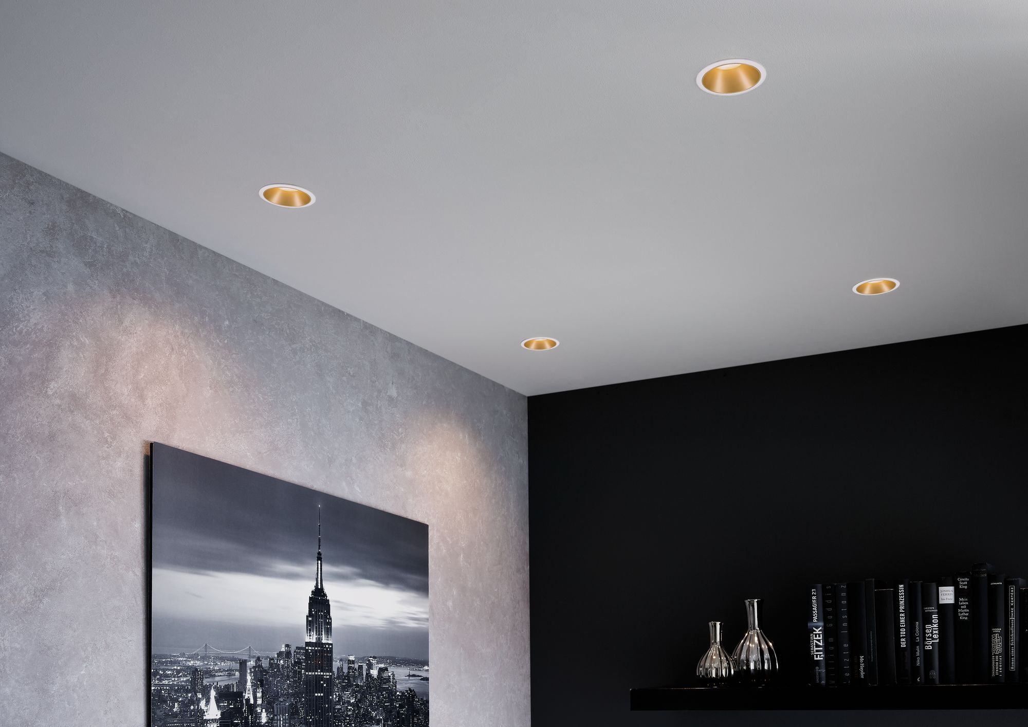 Four white recessed spotlights with gold reflector in modern living room with cityscape photo and bookshelf.