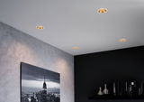 Four white recessed spotlights with gold reflector in modern living room with cityscape photo and bookshelf.