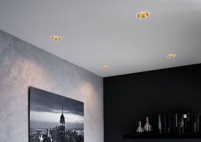 Four white recessed spotlights with gold reflector in modern living room with cityscape photo and bookshelf.