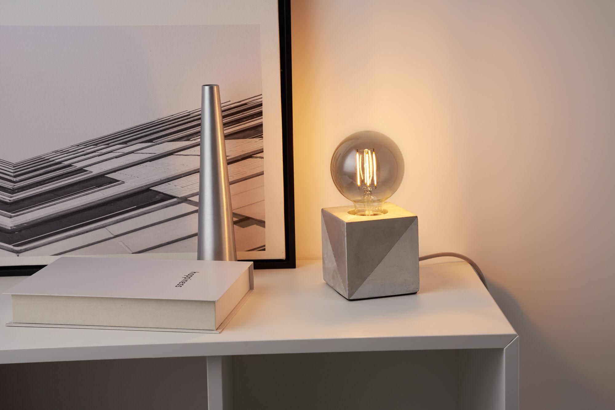Moderne bordlampe med grå betonfod og rund LED-pære på hvid hylde til boligbelysning