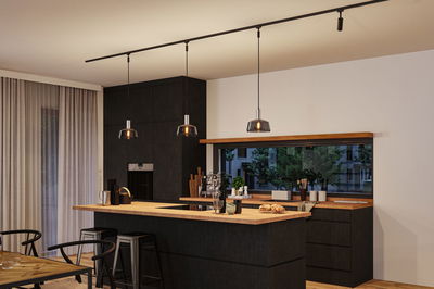 Moderne Küche mit schwarzer Holzoptik und Holzarbeitsplatte, drei Pendelleuchten und Barhockern