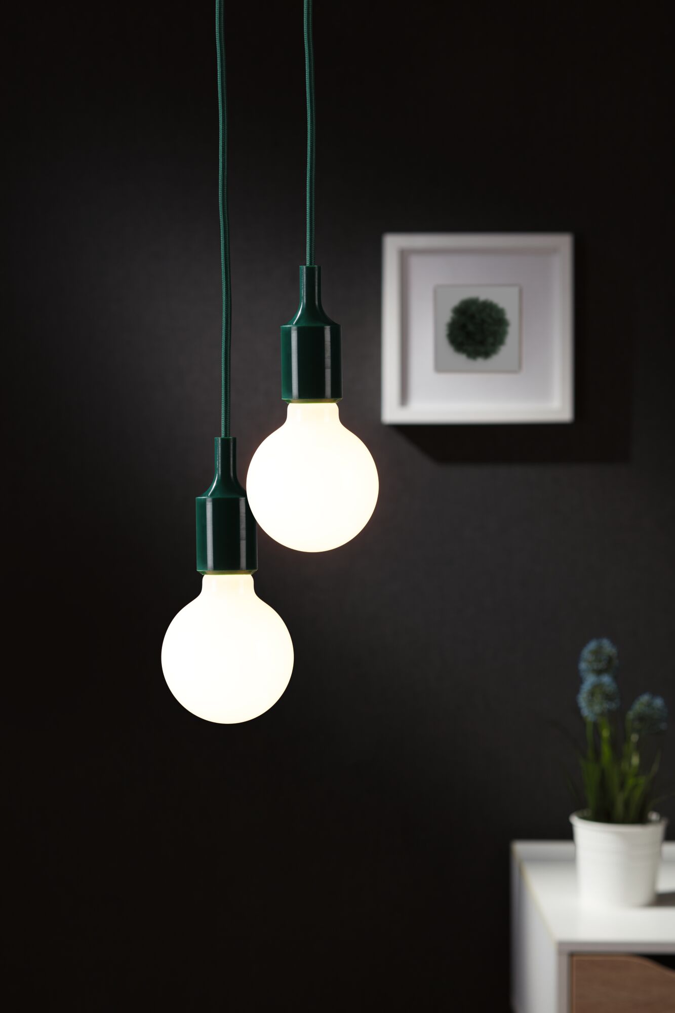 Zwei hängende LED-Glühbirnen mit grünem Kabel vor dunkler Wand, moderne Wohnraumbeleuchtung.