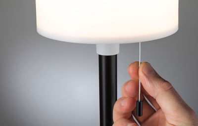 Main tirant une corde blanche sur un pied de lampe noir avec abat-jour blanc