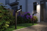 Modern black metal LED outdoor lights illuminate garden path with colorful flowers and house facade.