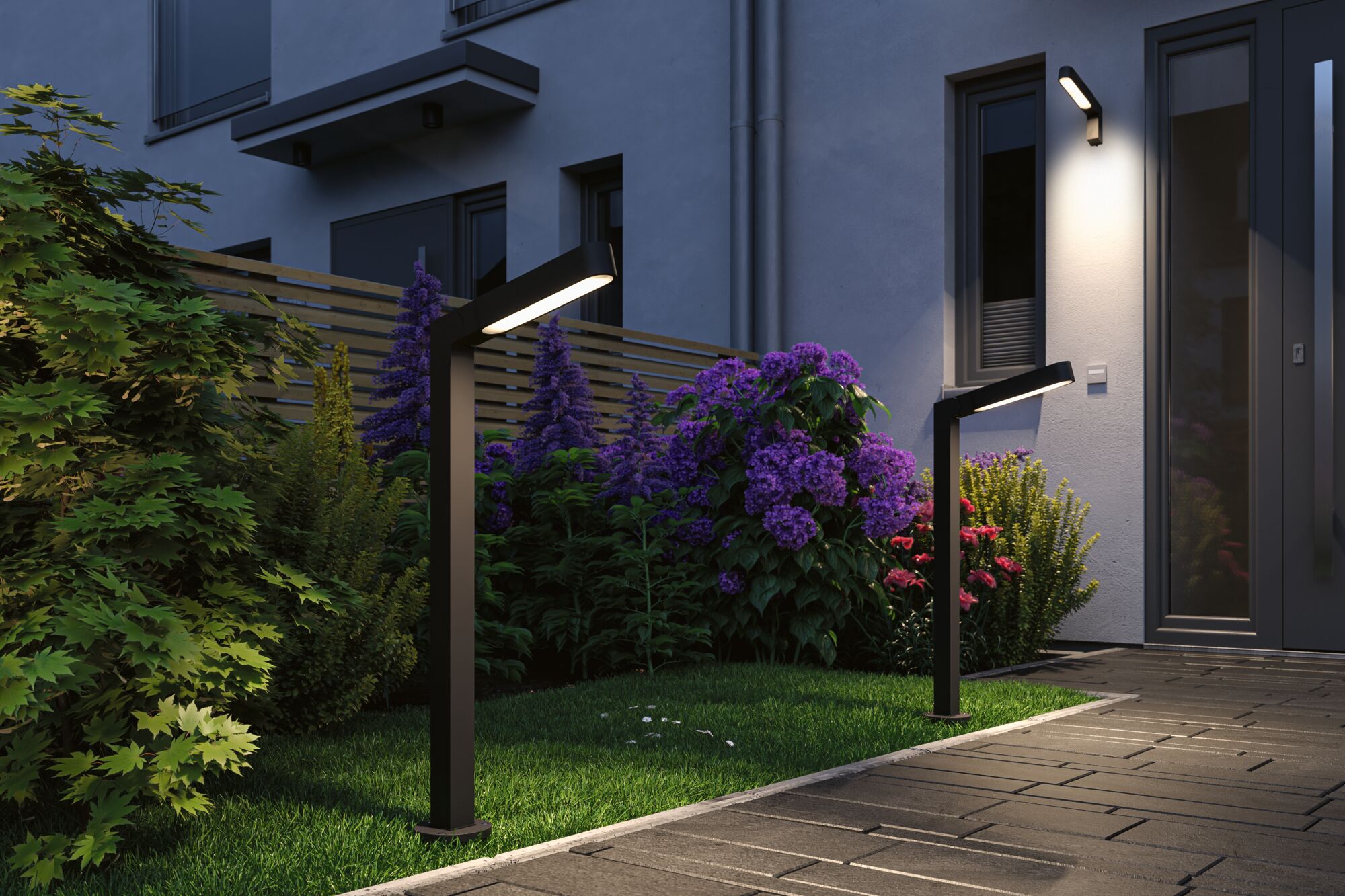 Moderne schwarze LED-Außenleuchten aus Metall beleuchten Gartenweg mit bunten Blumen und Hausfassade.