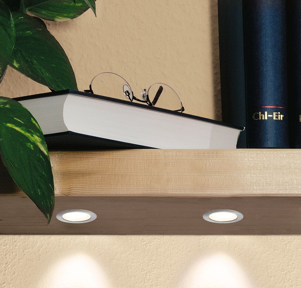 Two round LED recessed lights with silver aluminum frame under light wooden shelf with book and plant