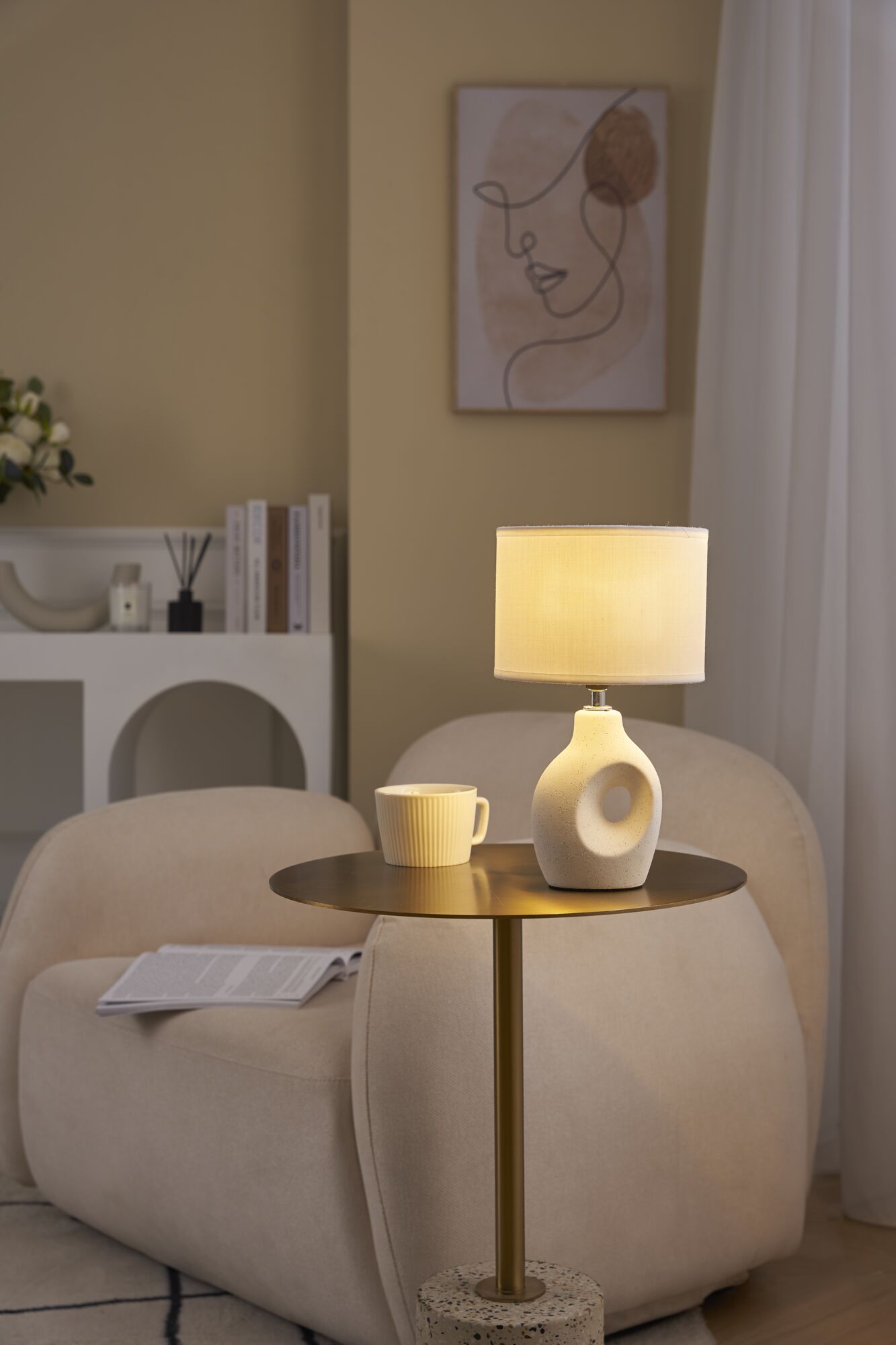 Beige bordlampe med stofskærm og keramisk fod på gyldent sidebord i stue.