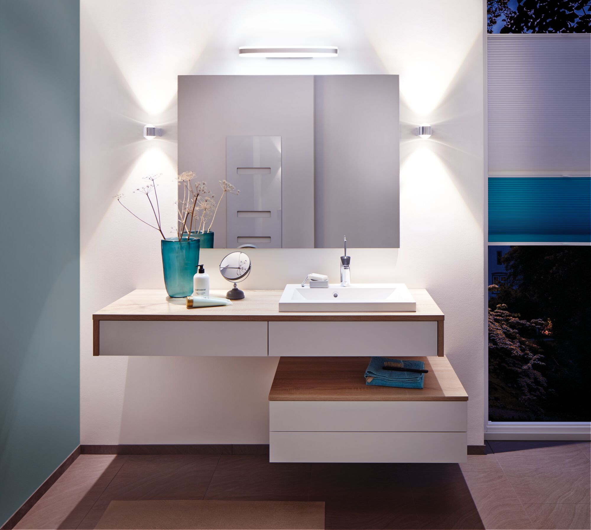 Modernes Badezimmer mit weißem Waschbecken, Holzarbeitsplatte und LED-Wandleuchten für stimmungsvolle Beleuchtung