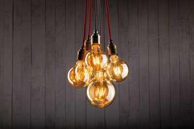 Five hanging warm light bulbs with red and black cords against a grey wooden wall background.