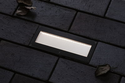 Rectangular LED recessed floor light with black metal frame on dark pavement, outdoor lighting
