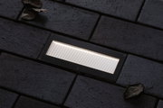 Rectangular black LED recessed light with white illumination on dark pavement for outdoor use