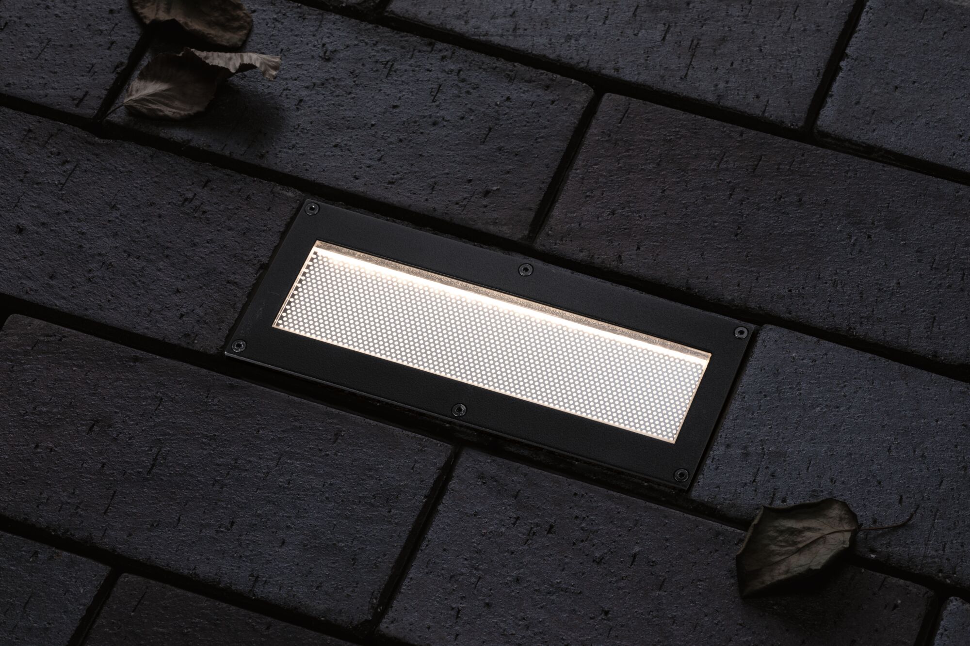 Rechthoekige zwarte LED-inbouwlamp met wit licht op donkere bestrating voor buitengebruik