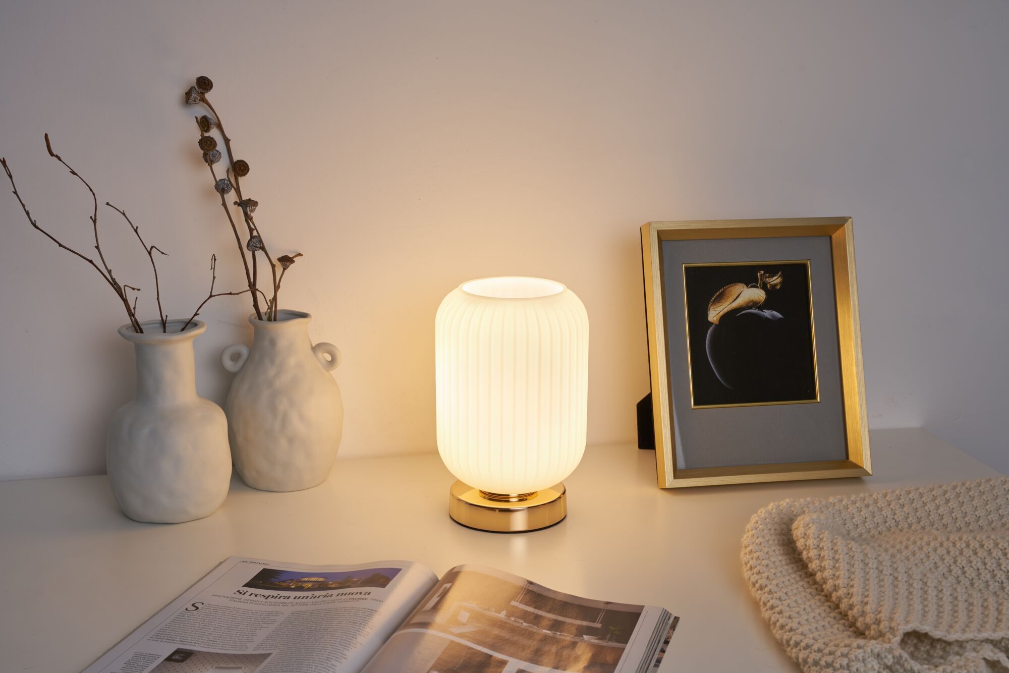 White ceramic vases with branches beside warm white table lamp with gold base for cozy lighting