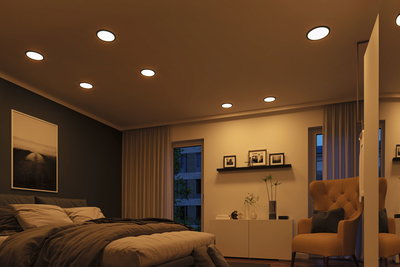 Chambre moderne avec spots LED encastrés blanc chaud au plafond et fauteuil marron confortable.