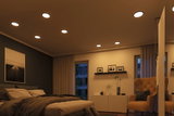 Chambre moderne avec spots LED encastrés blanc chaud au plafond et fauteuil marron confortable.