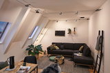 Modernes Wohnzimmer mit schwarzem Stoffsofa, grauem Teppich und Paulmann LED-Seilzugbeleuchtung an der Decke.