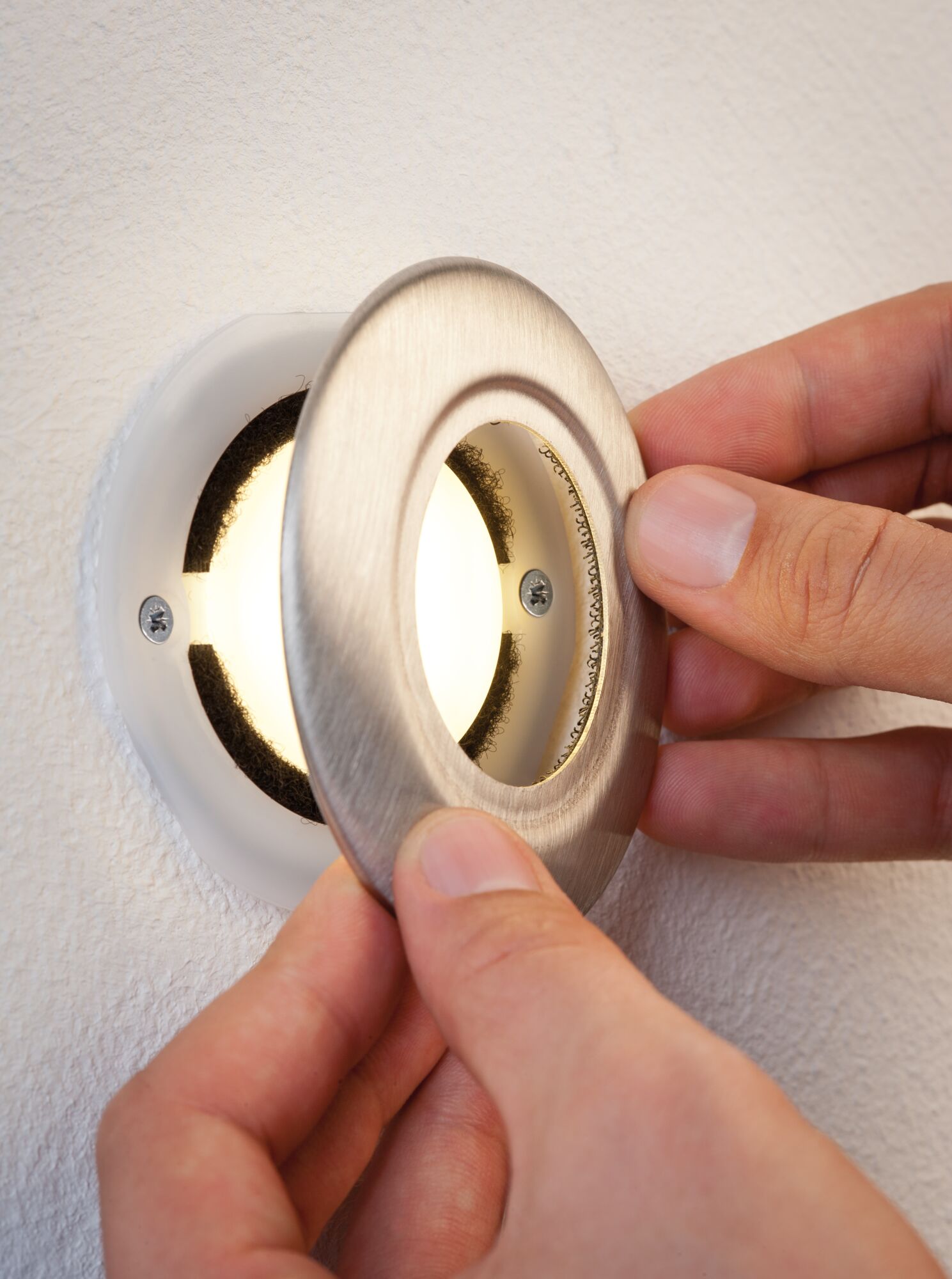 Hand installing round recessed LED spotlight with brushed stainless steel frame on white wall