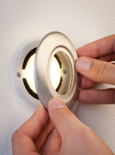 Hand plaatst ronde inbouw LED-spot met geborsteld roestvrijstalen frame op witte muur