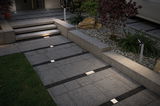 Modern outdoor lighting with recessed LED floor lights and bollard light on grey stone pathway.