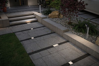 Modern outdoor lighting with recessed LED floor lights and bollard light on grey stone pathway.