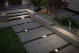 Moderne buitenverlichting met verzonken LED-vloerlampen en paaltjeslamp op grijs stenen pad.