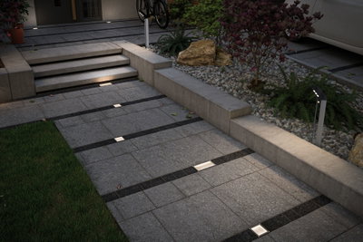 Moderne buitenverlichting met verzonken LED-vloerlampen en paaltjeslamp op grijs stenen pad.