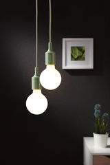 Two hanging LED bulbs with green sockets against black wall and white table with plant indoors.