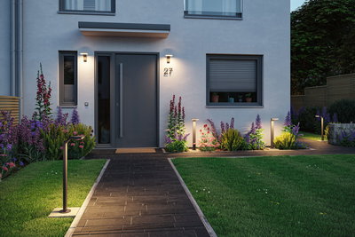 Modern outdoor lighting with black LED path lights and wall lamps on house facade and garden path.