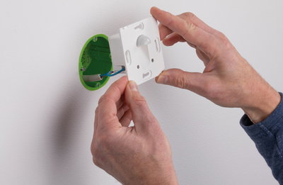 Installation eines weißen Bewegungsmelders mit grünem Unterputzgehäuse an weißer Wand für smarte Beleuchtung