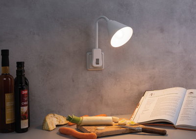 Weiße flexible LED-Wandleuchte mit Schalter beleuchtet Küchenarbeitsfläche mit Gemüse und Kochbuch.