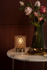 Glass table lamp with round pattern and warm light on marble top next to green vase with pink roses